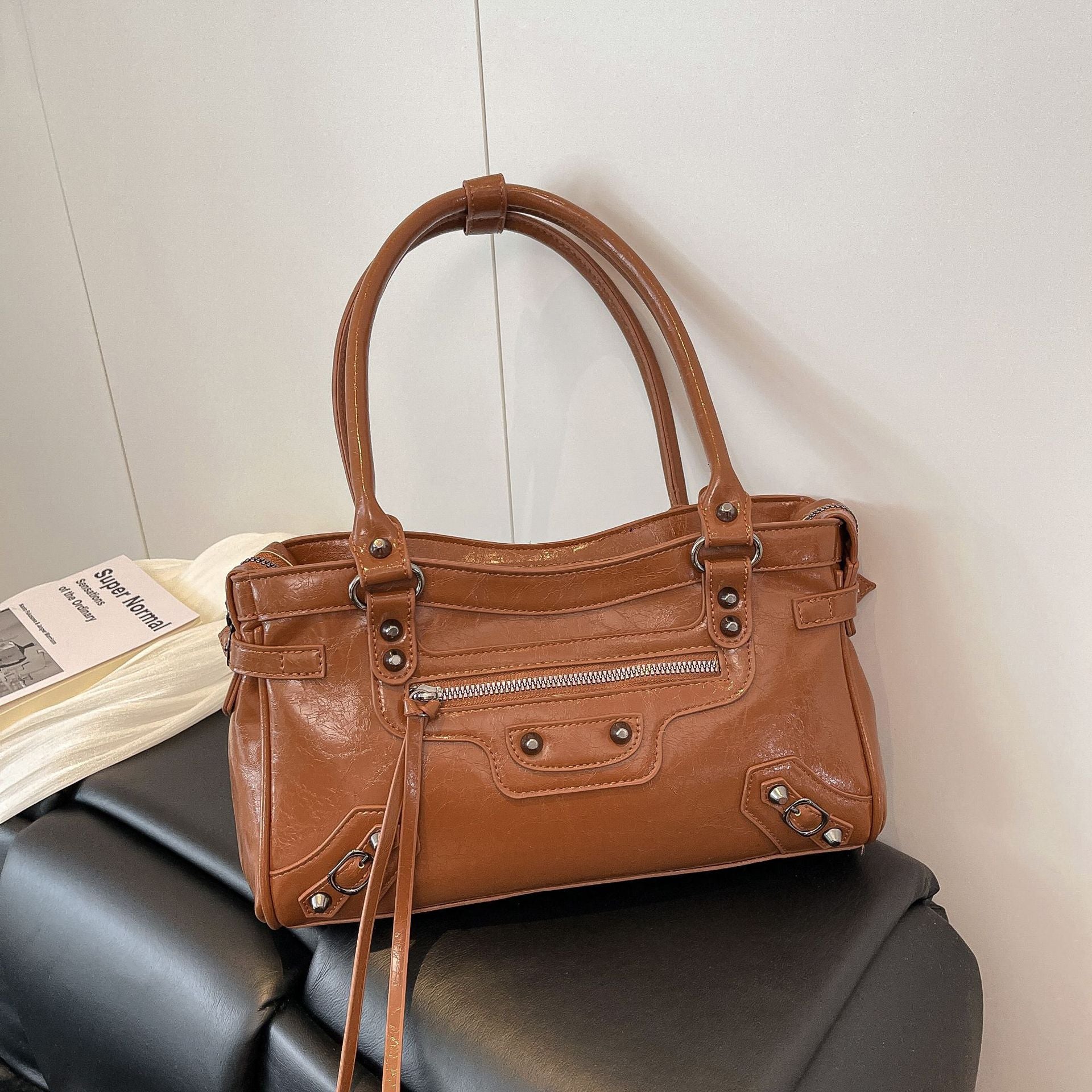 Brown leather handbag on a black surface with an open book in the background